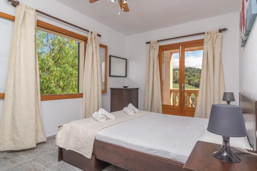 A bedroom with a double bed, curtained windows, and a glass door opening onto a balcony.