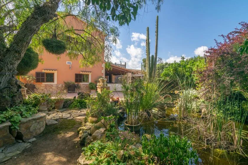 A landscaped garden with a small pond beside a peach-colored building.
