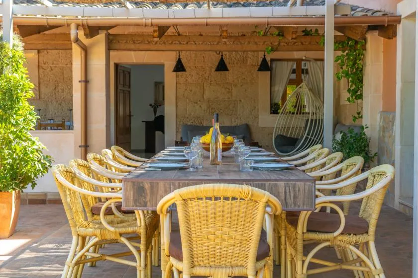 An outdoor dining area with a long table and wicker seating beneath a covered patio.