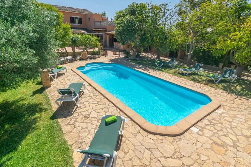Una piscina está en un jardín pavimentado con piedra junto a una casa.