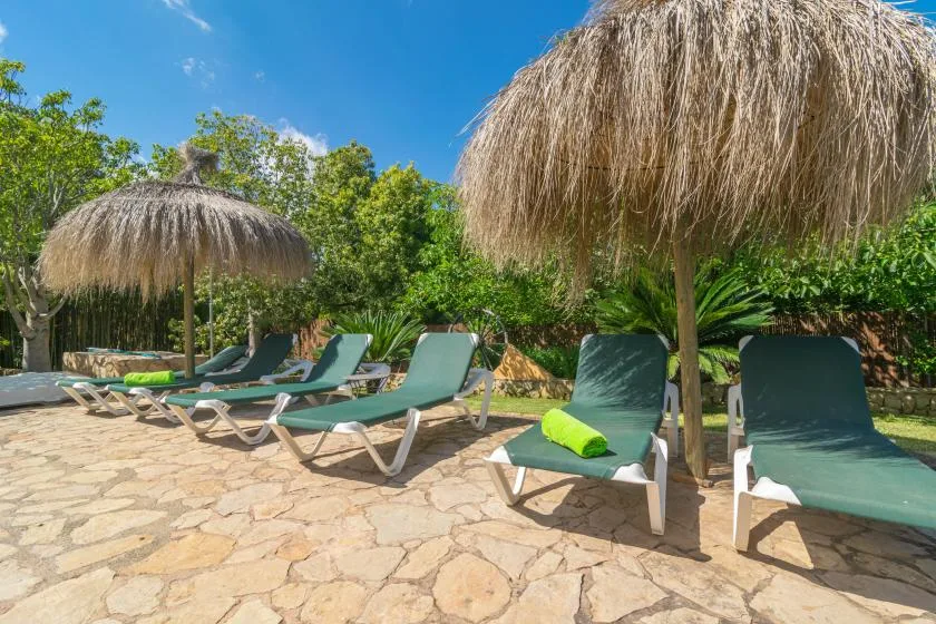 Una zona exterior de descanso junto a la piscina tiene tumbonas bajo sombrillas de paja.