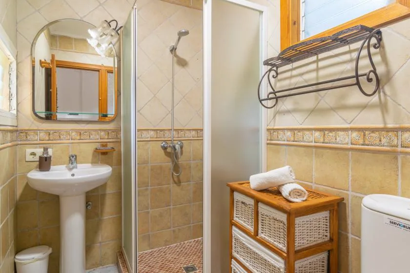 A tiled bathroom with a sink, shower, and wicker storage cabinet.