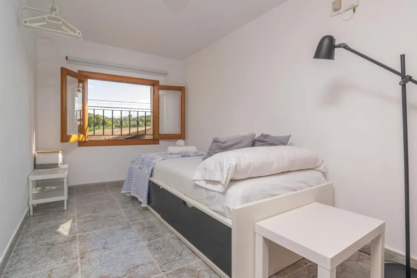 A bright bedroom with a bed beside an open window.