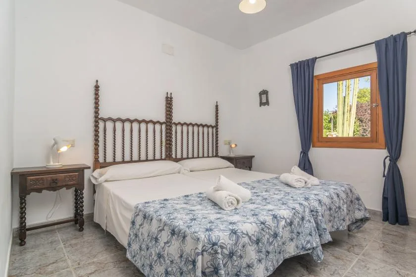 A bedroom with two beds, floral bedding, and a window with blue curtains.