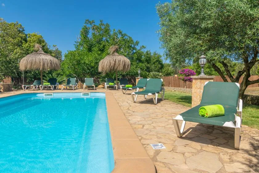 An outdoor swimming pool is surrounded by stone paving and lounge seating.