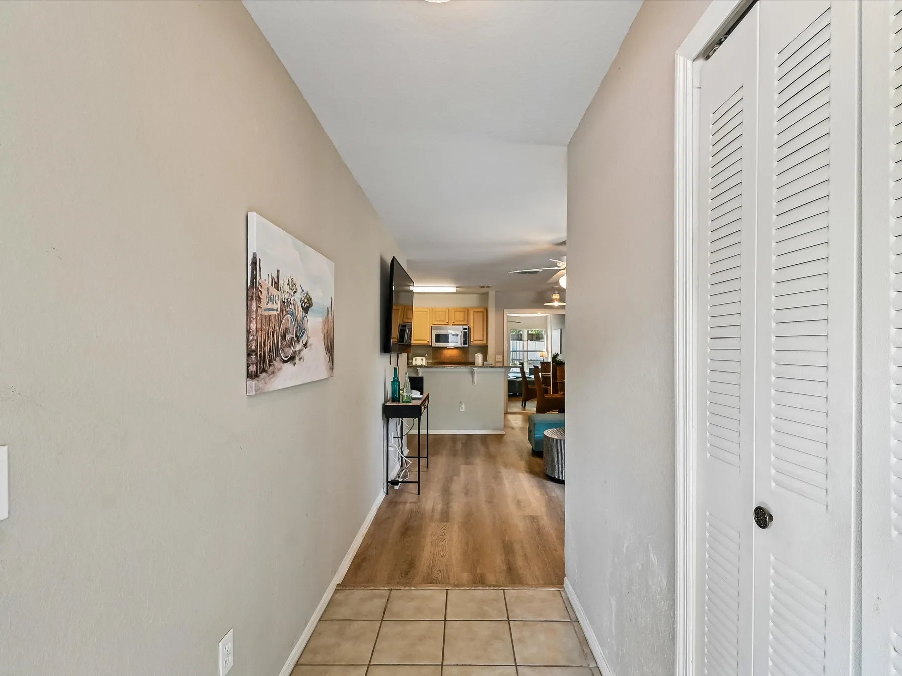 A hallway opens into a living area with wood flooring and a kitchen beyond.