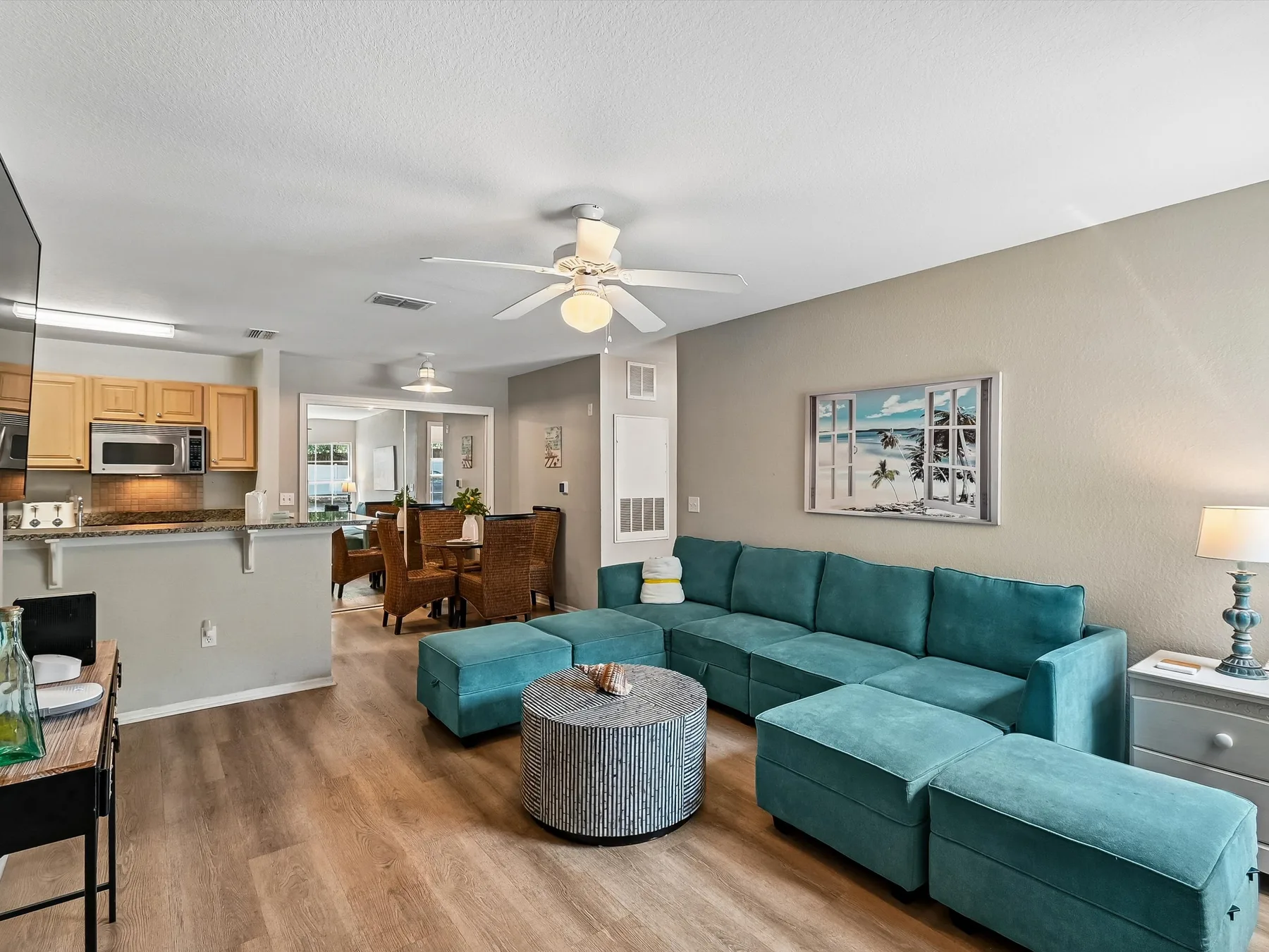 An open-plan living room with teal seating beside a kitchen and dining area.