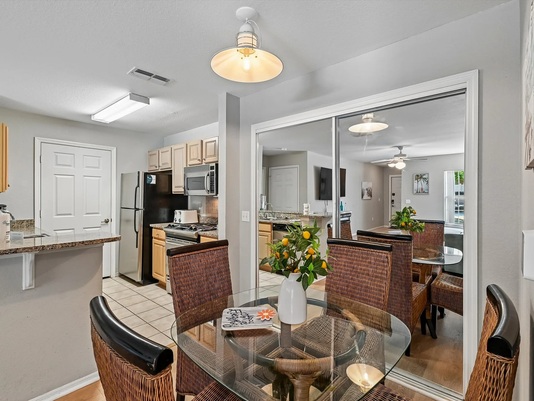 A dining area with a round glass table and woven chairs sits beside the kitchen.