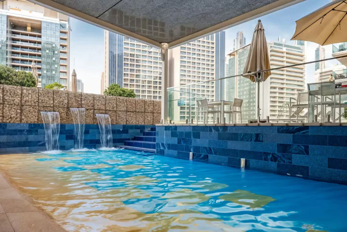 Una piscina en la azotea con paredes de azulejos azules y edificios de la ciudad al fondo.