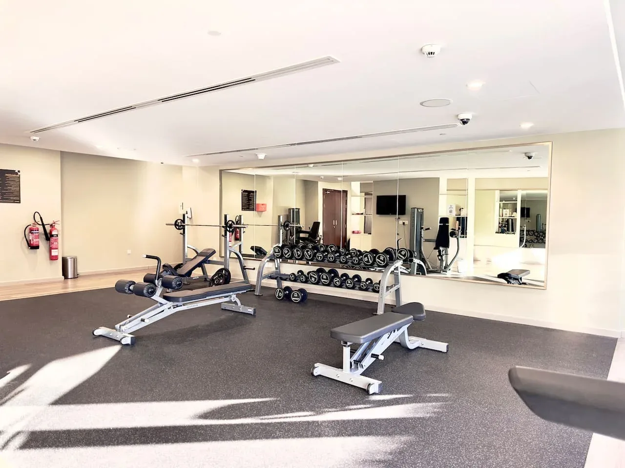 Una sala de fitness con pesas, máquinas de ejercicio y bancos frente a una pared con espejos.