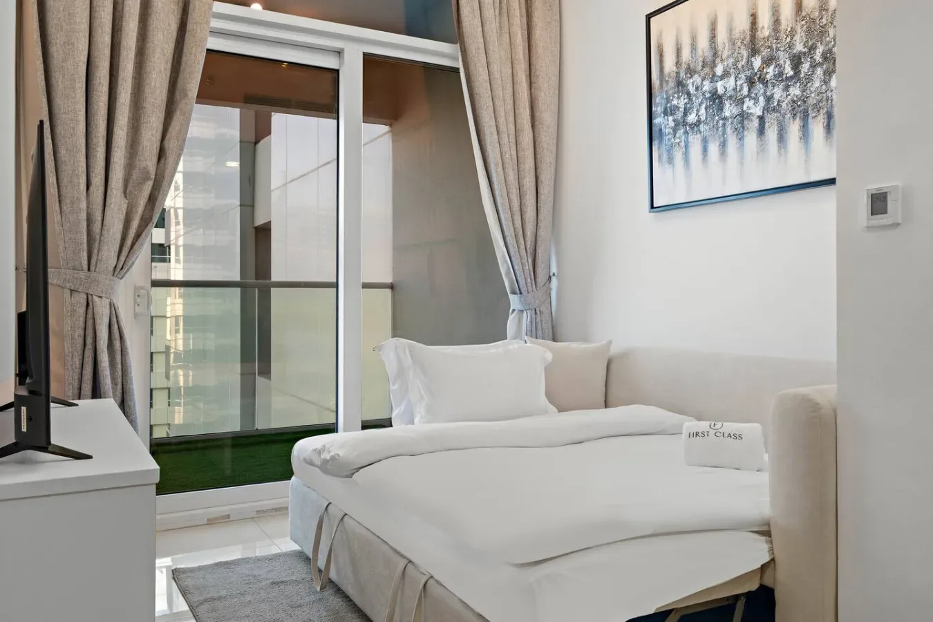 Un dormitorio con una cama bien tendida junto a una puerta de vidrio al balcón.