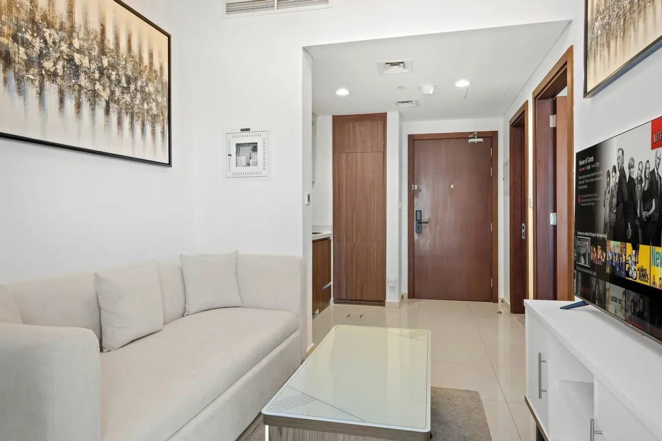 Una sala luminosa con asientos claros, una mesa de centro de vidrio y puertas de madera.