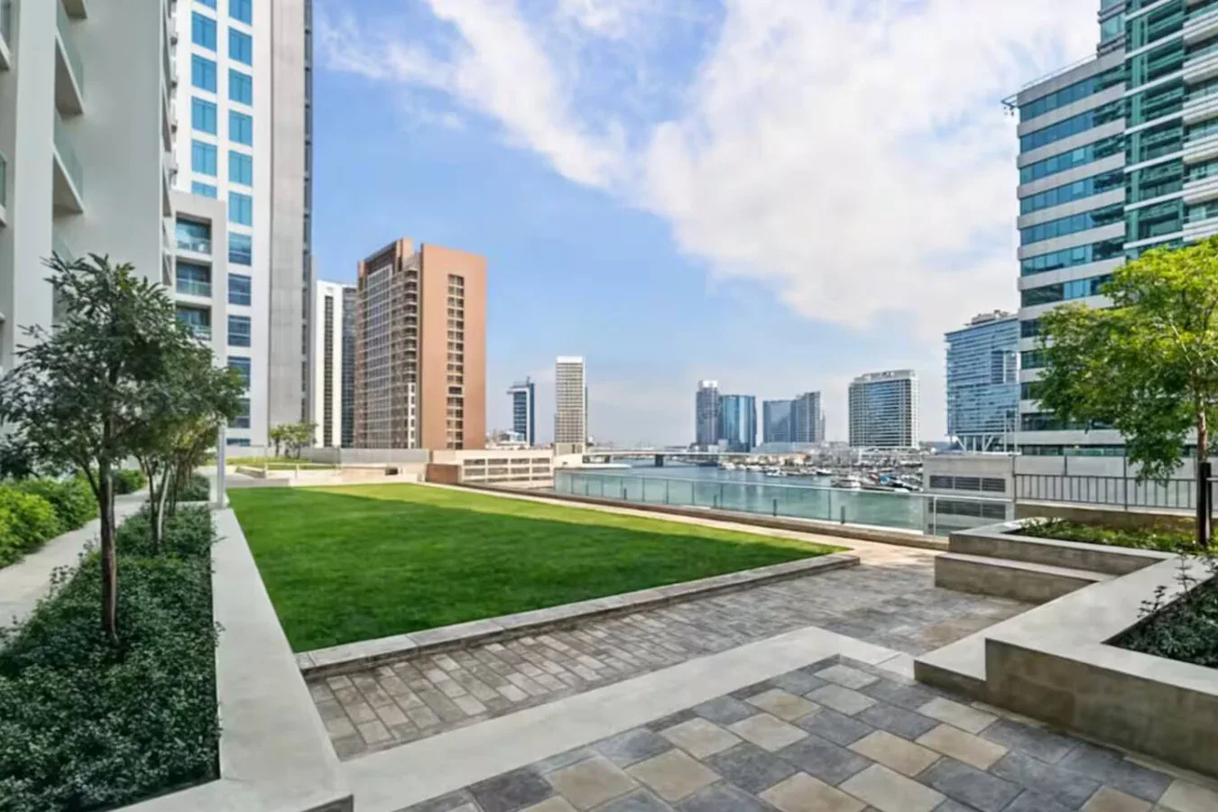 Una terraza ajardinada con césped verde da a la costa y a edificios de la ciudad.