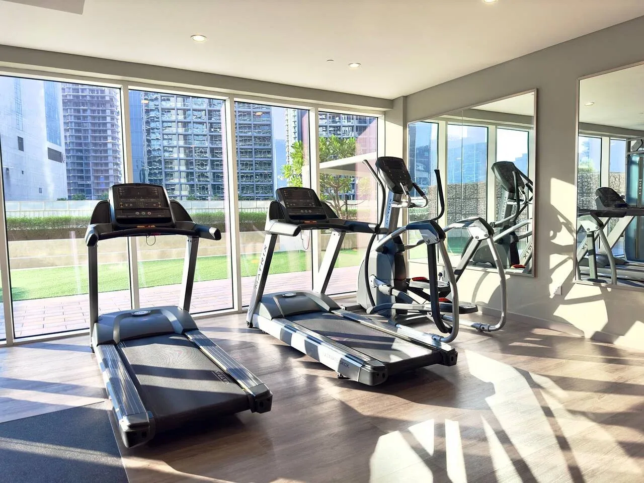Un gimnasio luminoso con cintas de correr y otras máquinas de ejercicio junto a grandes ventanas.