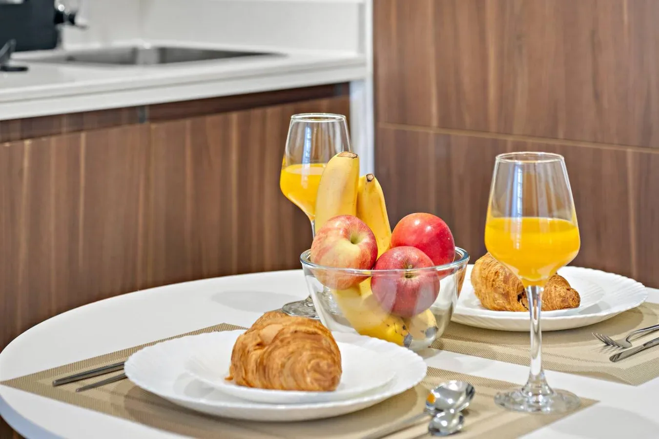 Una mesa está puesta con fruta, bollería y vasos de zumo de naranja.