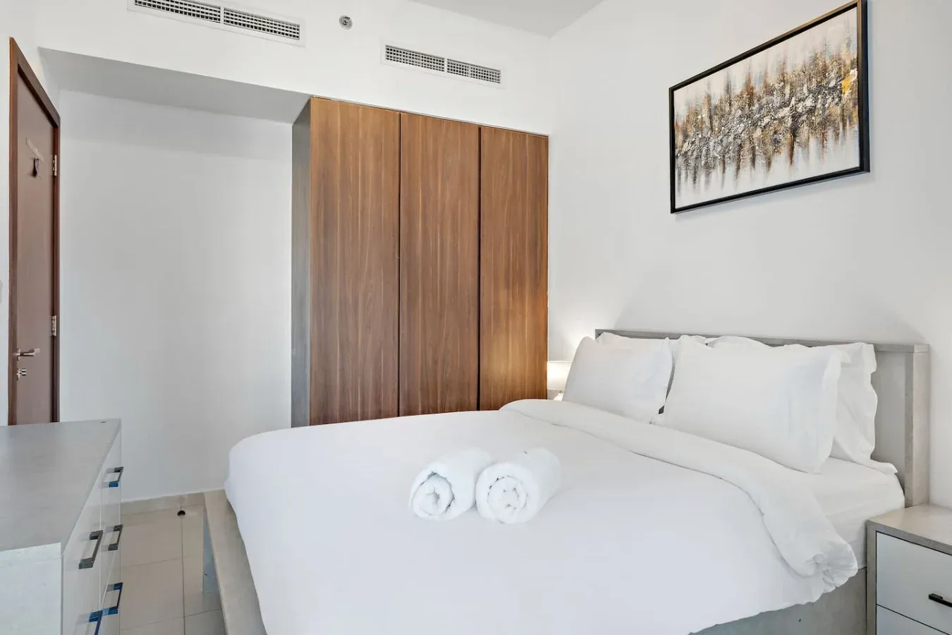 Un dormitorio luminoso con una cama bien hecha y un cuadro enmarcado encima.