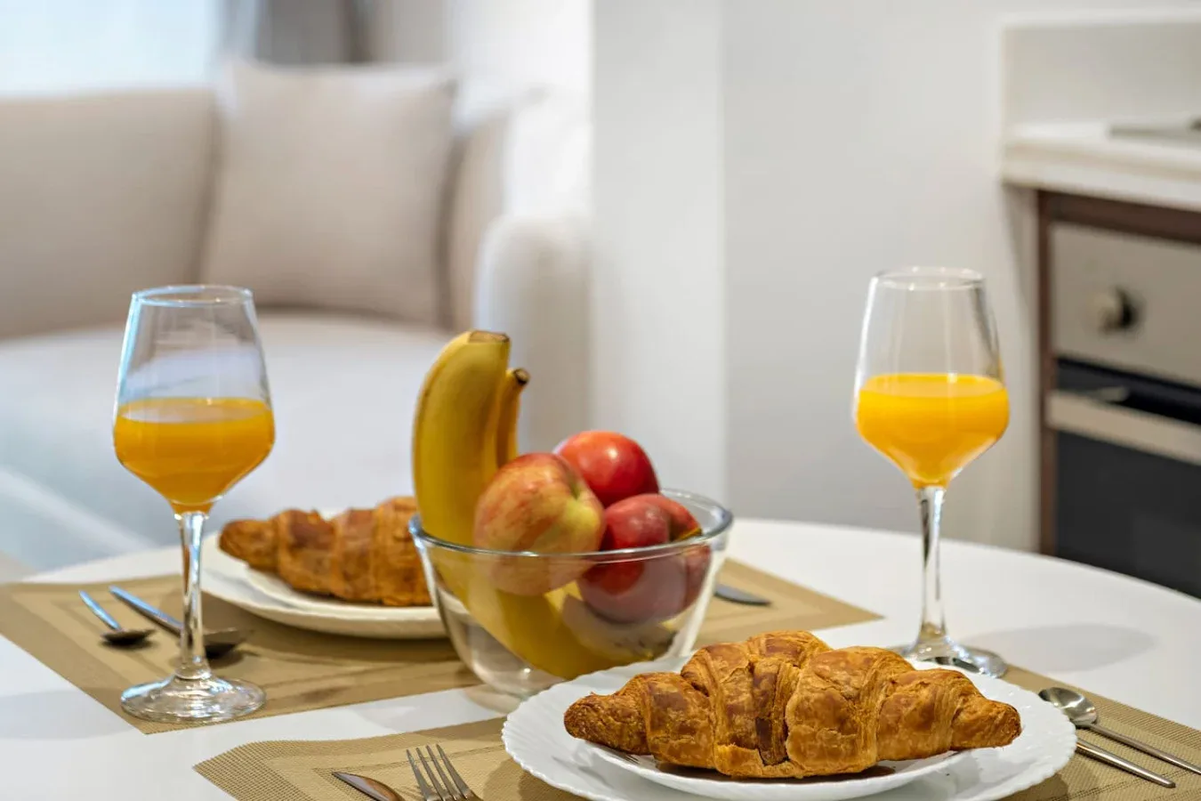 Una mesa de comedor con cruasanes, fruta y vasos de jugo de naranja.