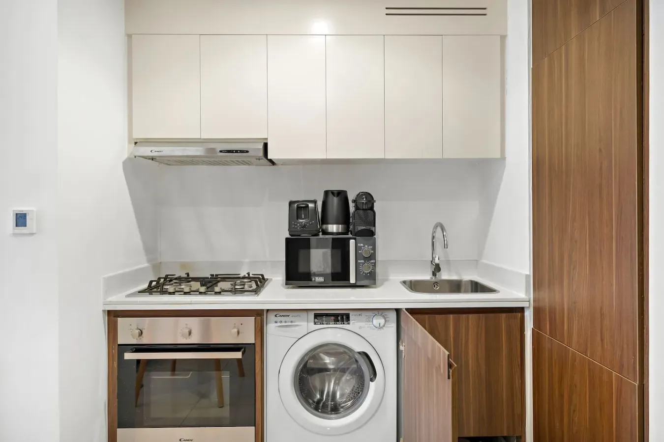 Una cocina compacta con gabinetes blancos, una placa de cocina, horno y lavadora.