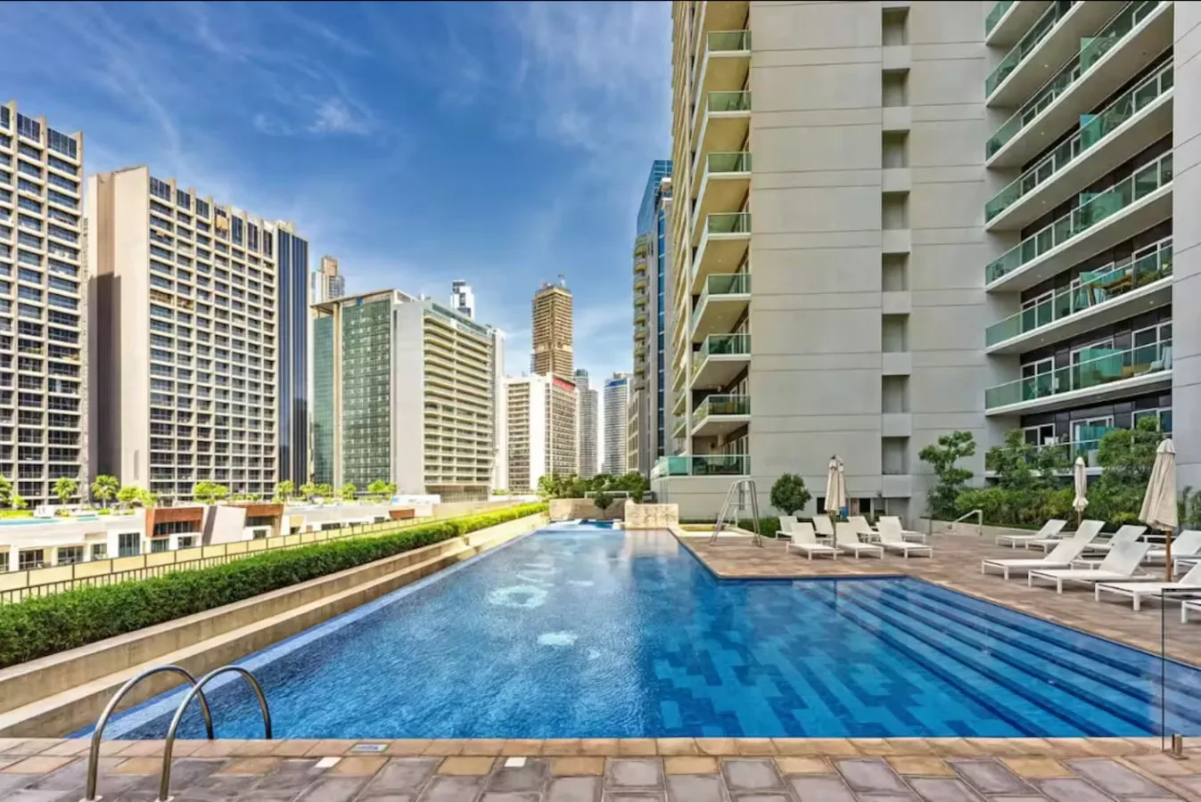Una piscina exterior está junto a edificios altos, con asientos de descanso en la terraza.