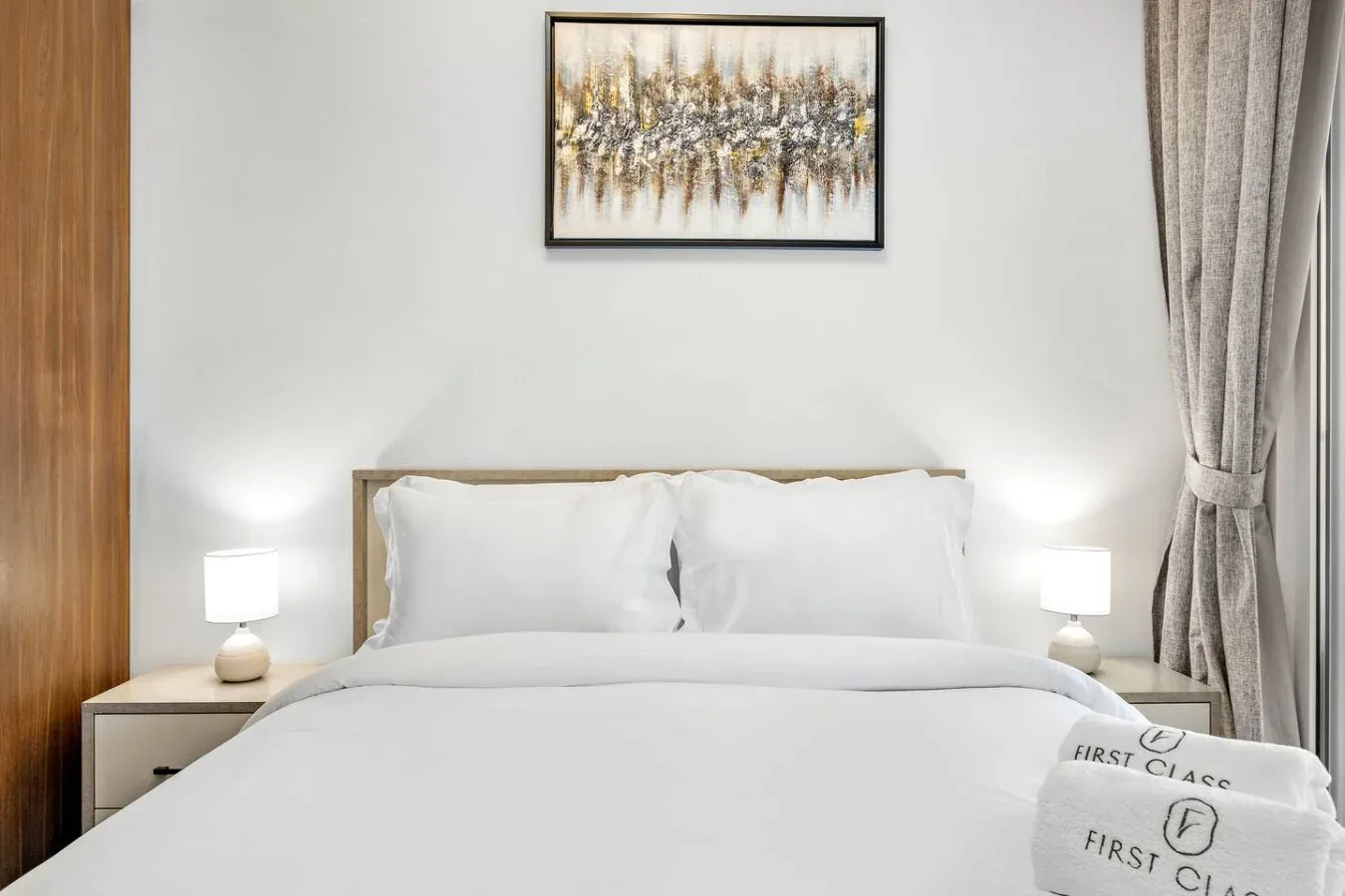 Un dormitorio con una cama tendida, lámparas de noche y un cuadro enmarcado.
