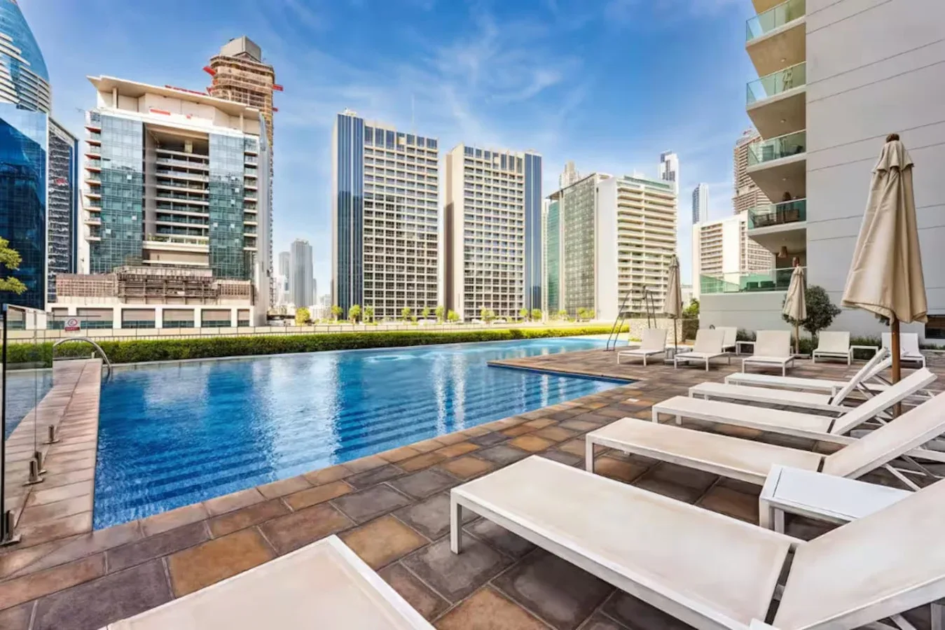 Una piscina al aire libre con tumbonas y edificios altos al fondo.
