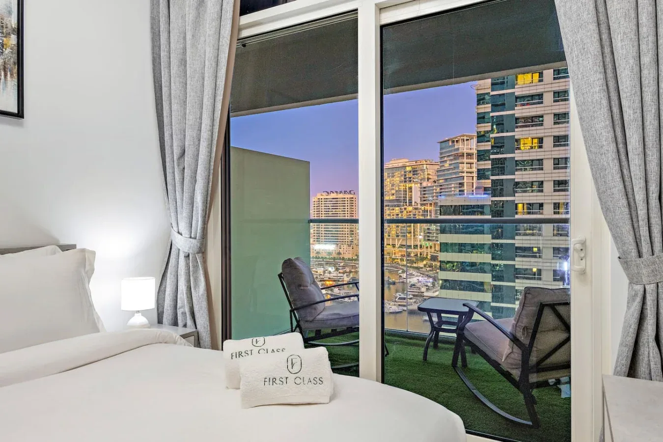 Un dormitorio da a un balcón con asientos y vistas de edificios cercanos.