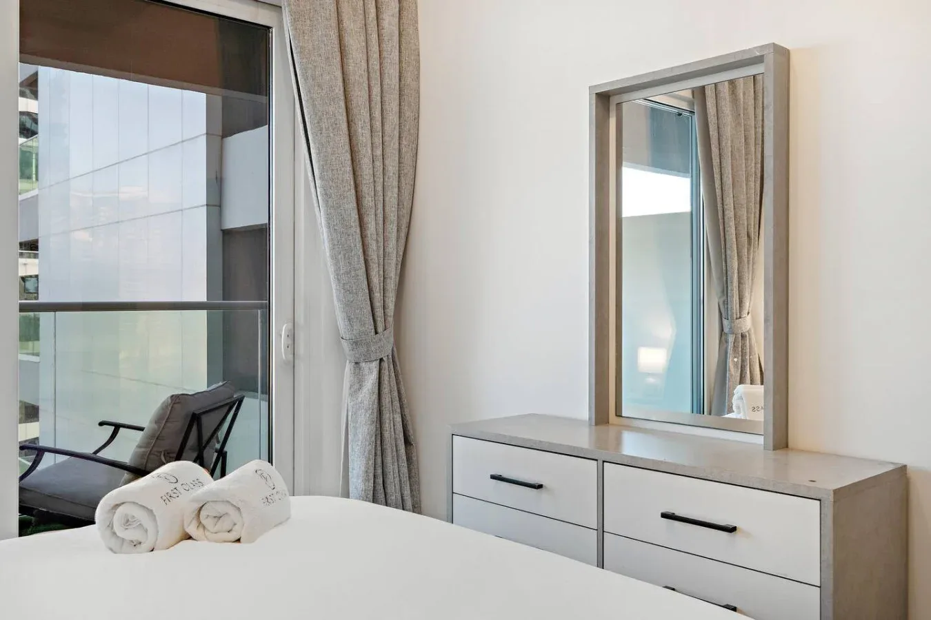 Dormitorio con cama, ventanas con cortinas y una cómoda con espejo.