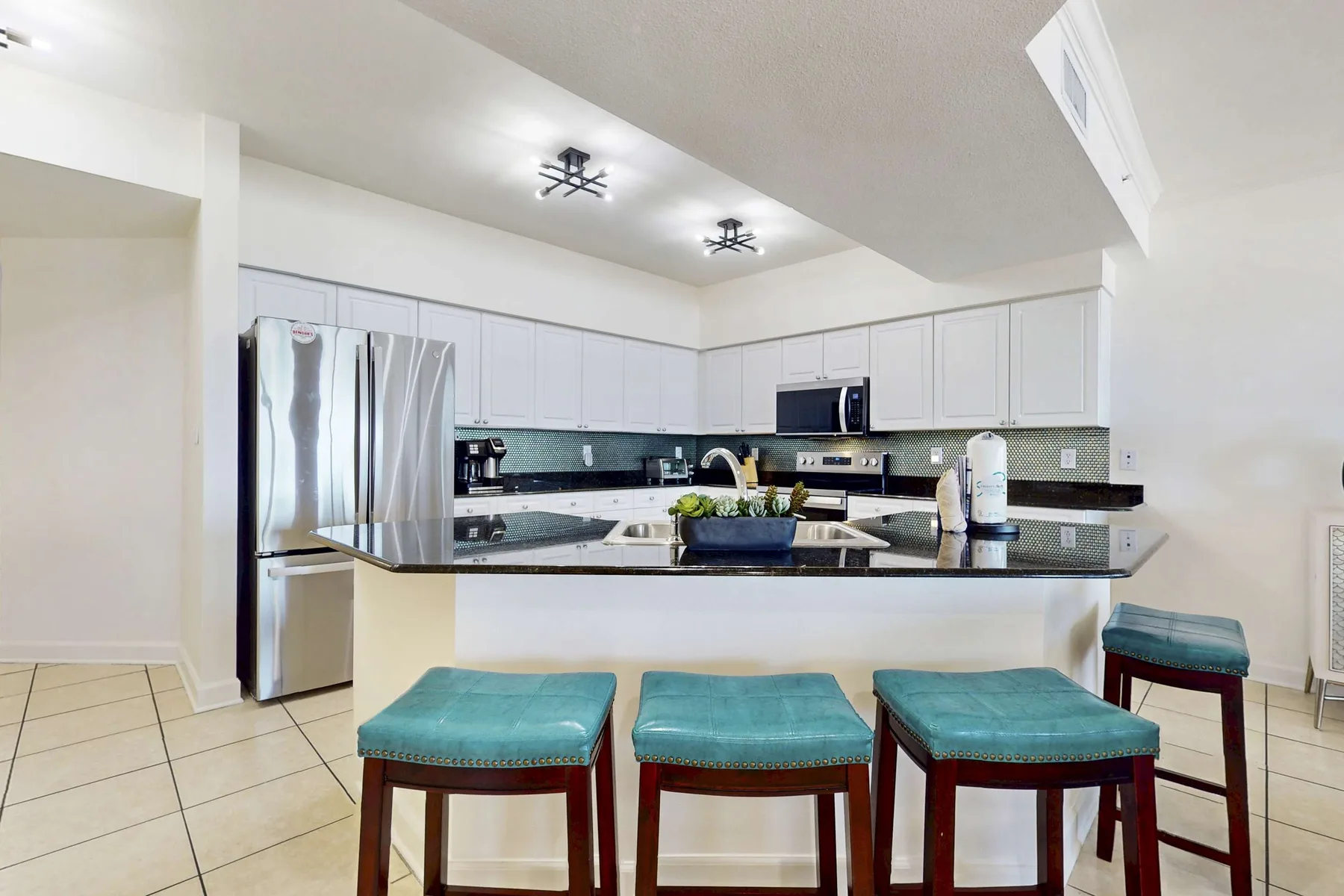 A bright kitchen with white cabinets, a central island, and turquoise seating.