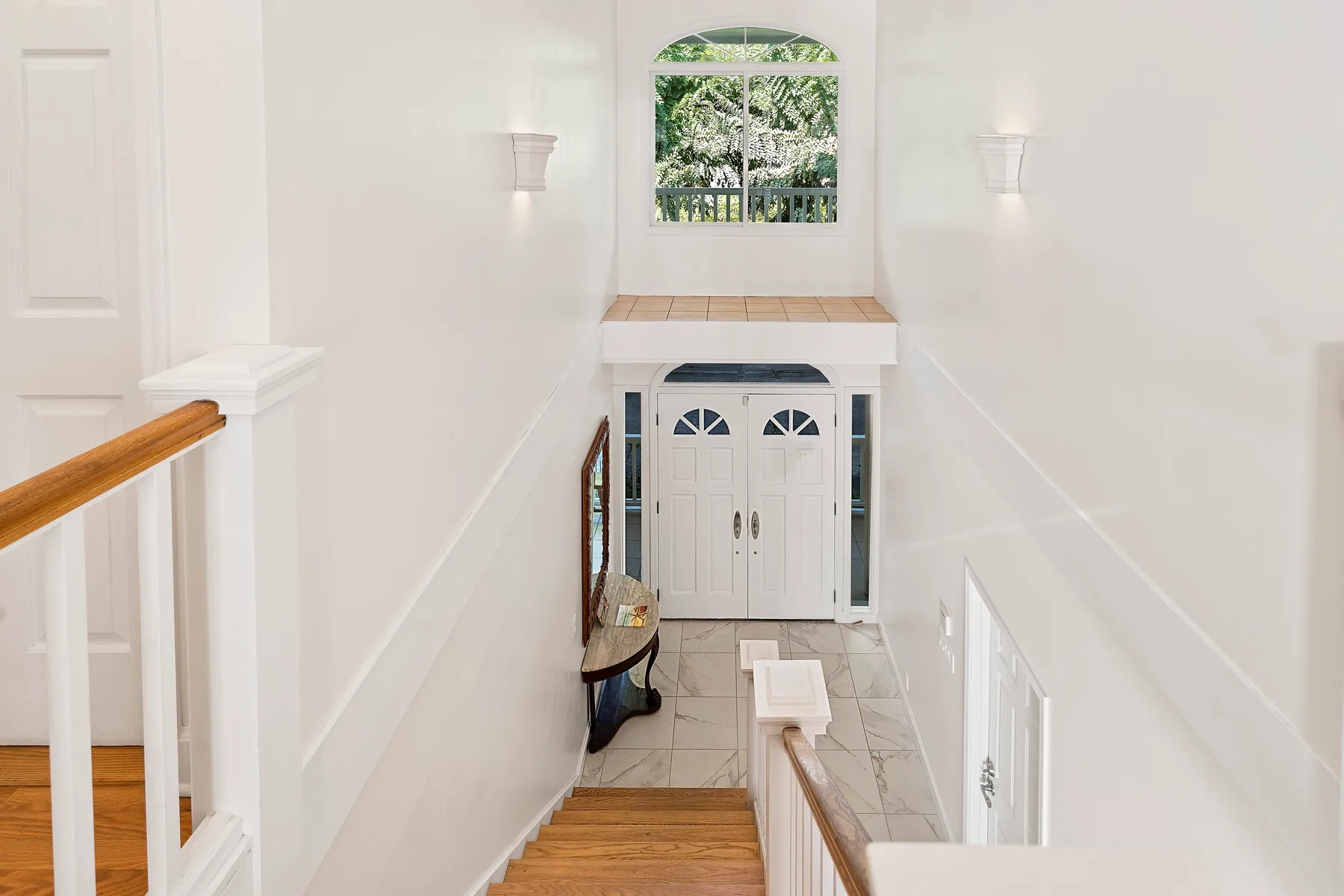 Una escalera blanca y luminosa conduce a un pequeño descanso bajo una ventana.
