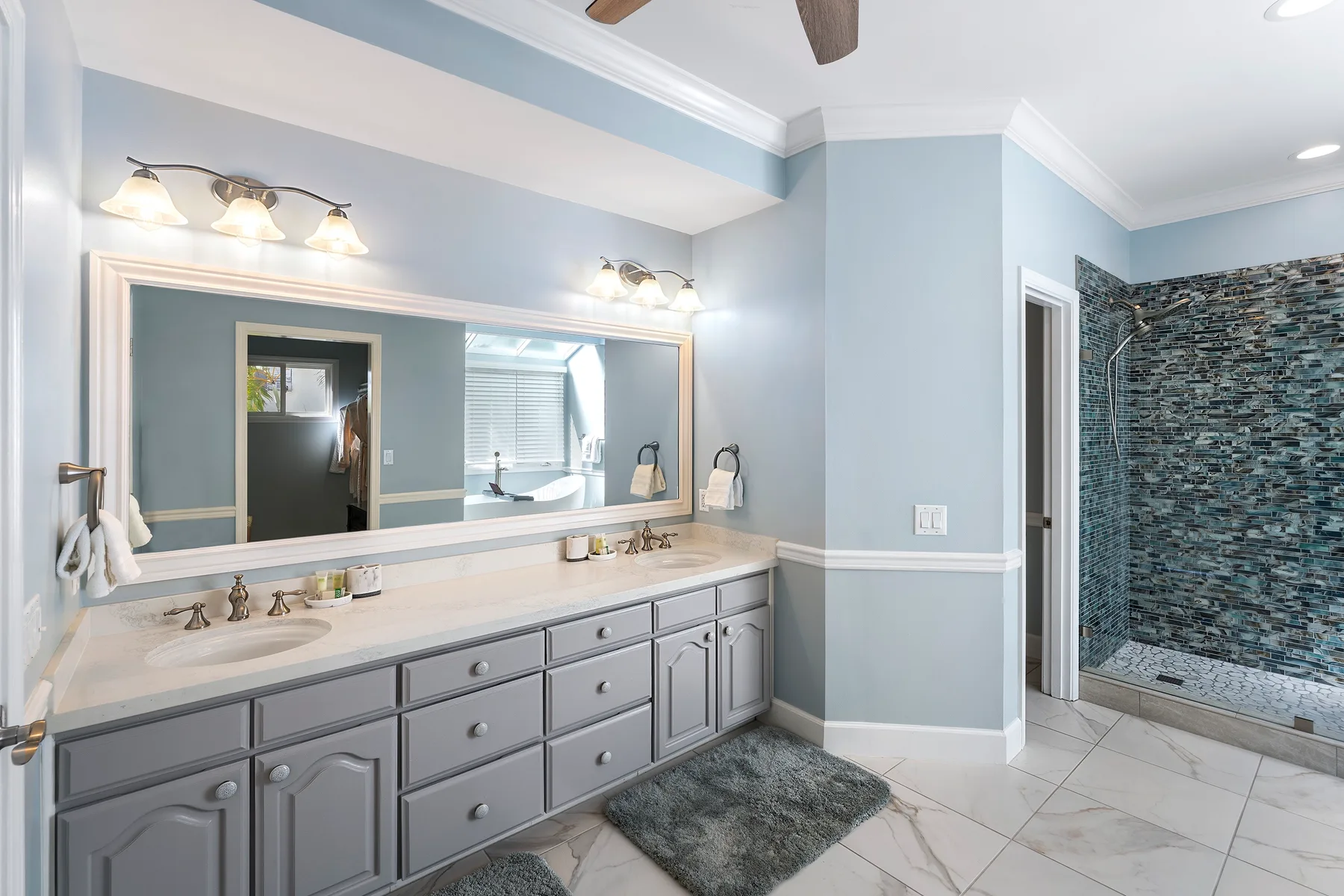 Un tocador de baño con un espejo amplio está junto a una ducha revestida de azulejos.