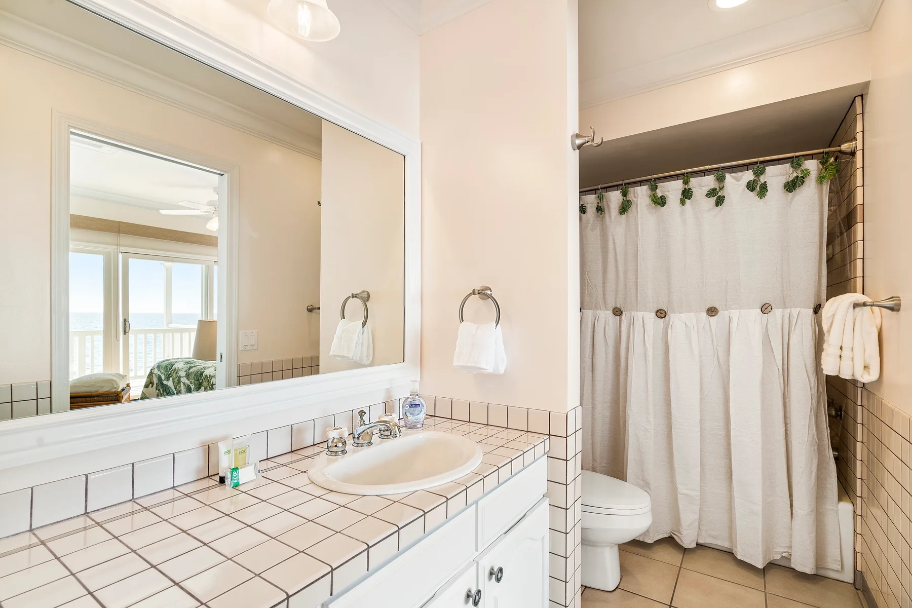 Un baño luminoso con lavabo alicatado, espejo y ducha con cortina.