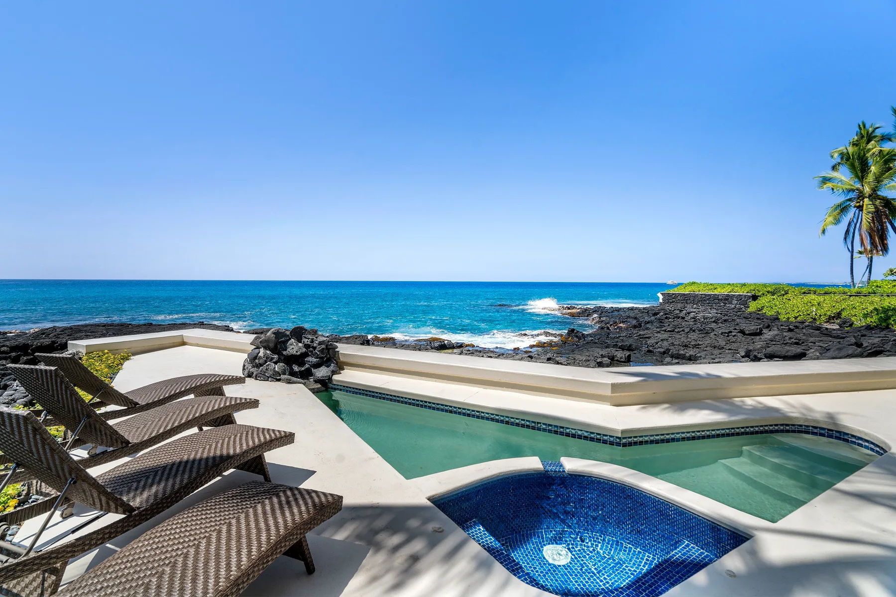 Una piscina y un spa junto al mar miran al océano, con tumbonas cerca.