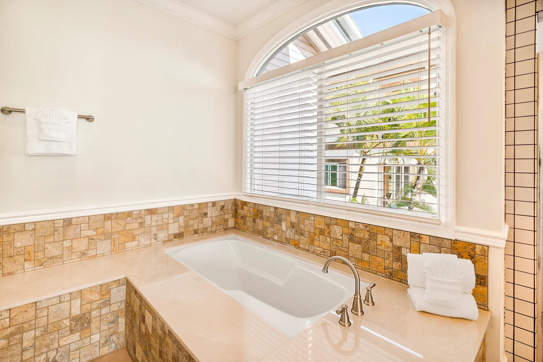 Un baño luminoso con una bañera empotrada bajo una gran ventana arqueada.