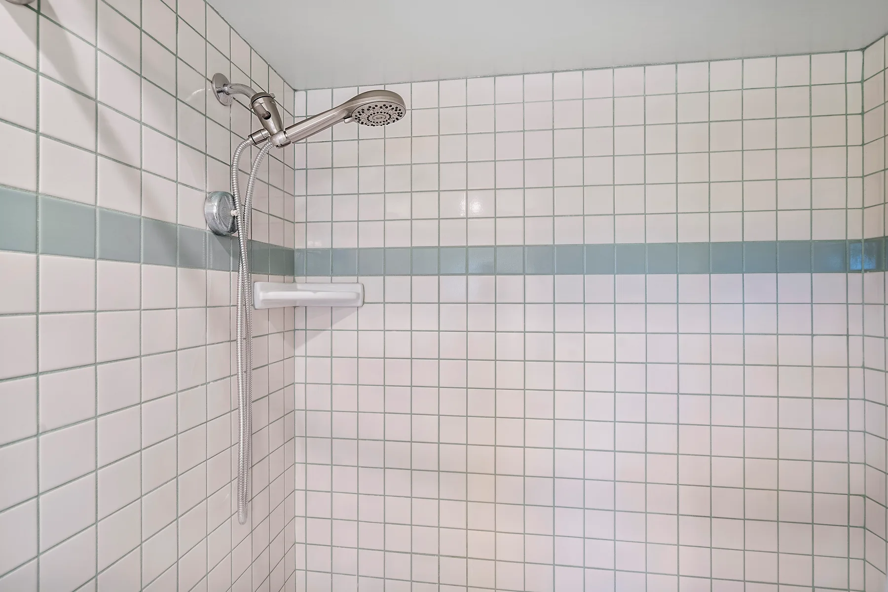 Una ducha alicatada con ducha de mano y una franja horizontal azul grisácea.