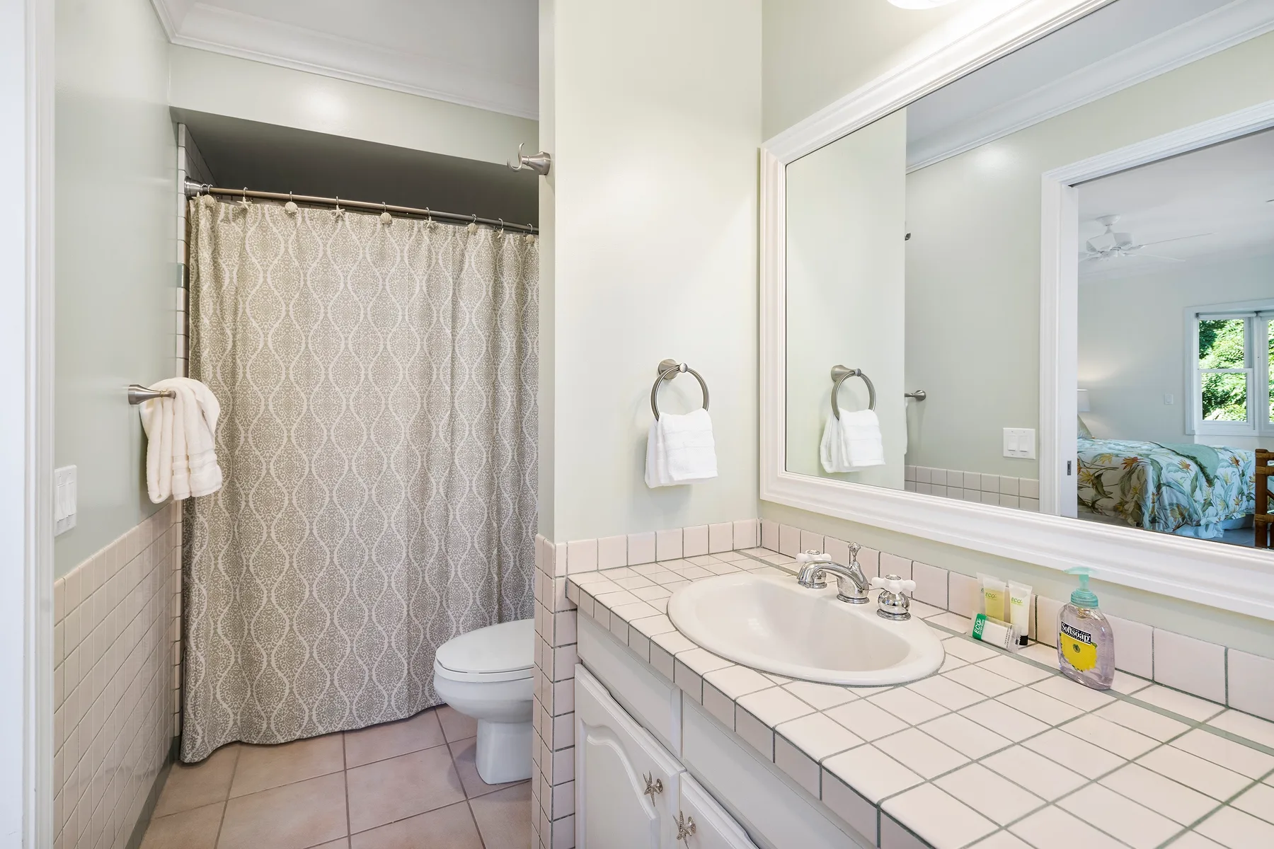 Un baño con lavabo y encimera de azulejos y una cortina de ducha estampada.