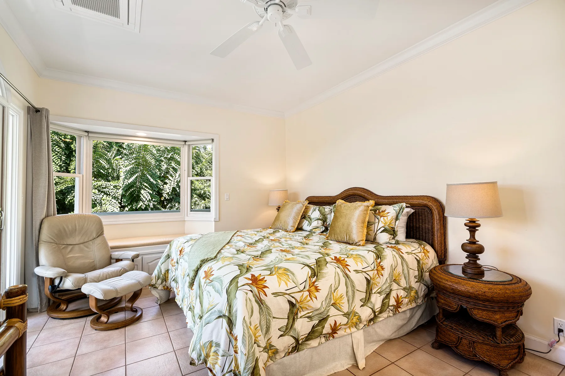 Un dormitorio con una colcha floral y una ventana con vistas a la vegetación.
