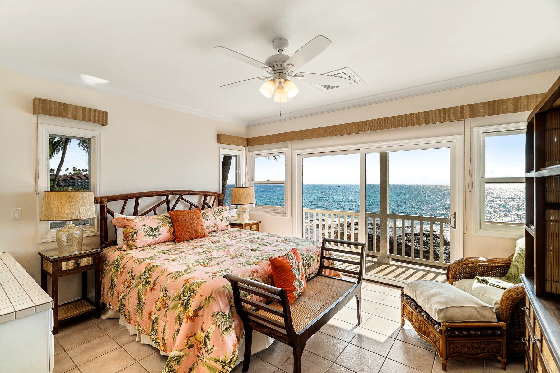 Un dormitorio con una colcha floral, asientos y grandes ventanas con vista al mar.