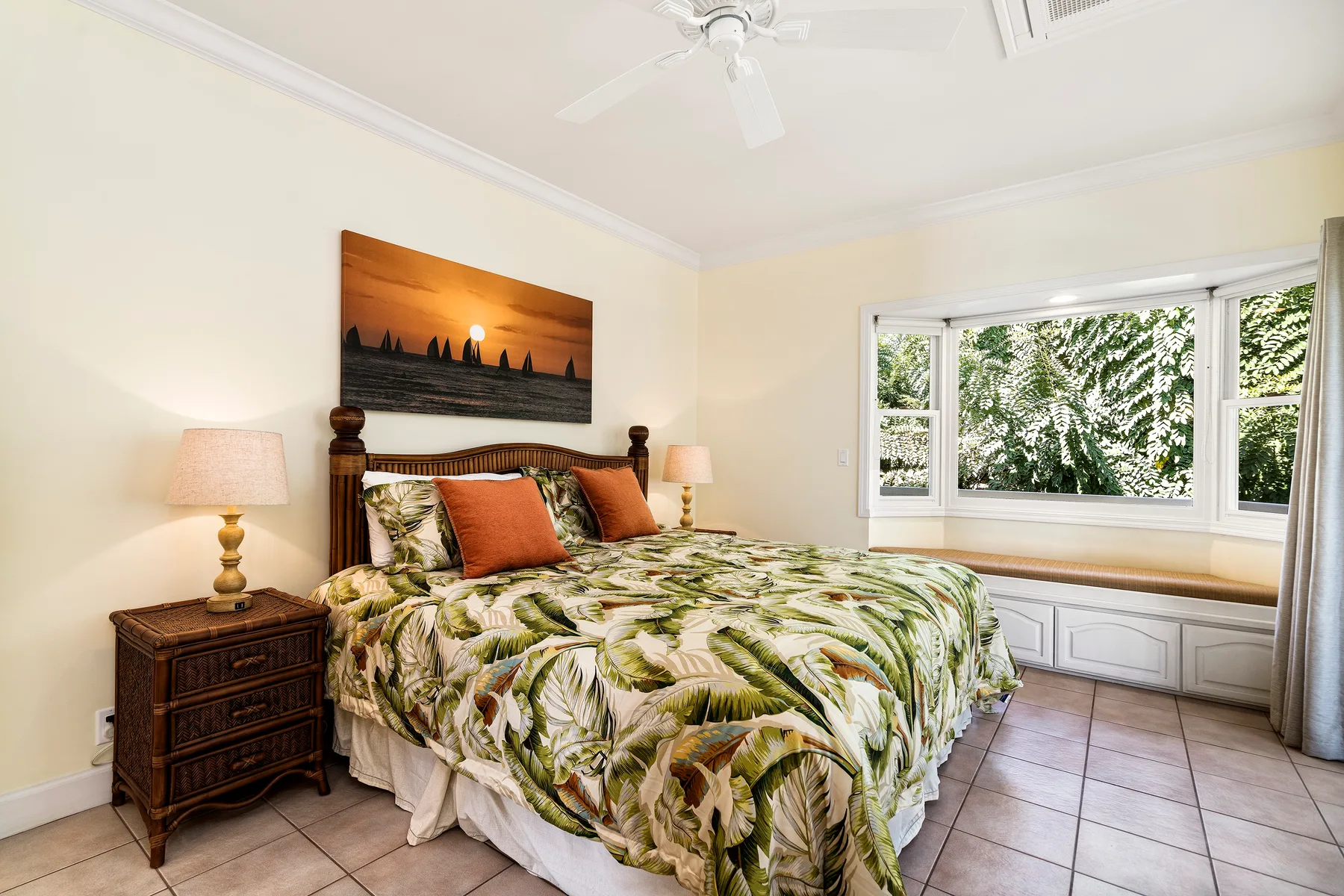 Dormitorio con una cama cubierta de ropa de cama estampada con hojas junto a una ventana grande.