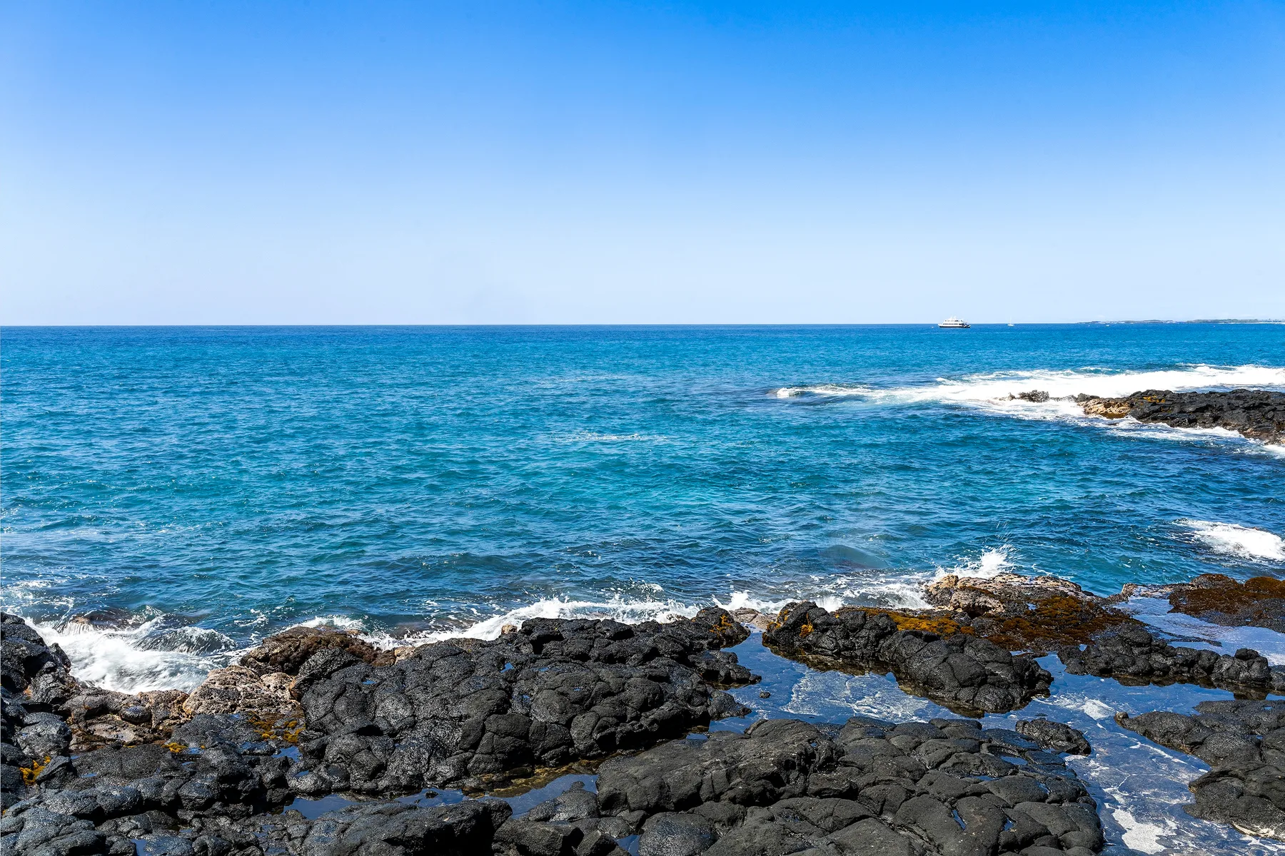 Costa rocosa con olas rompiendo sobre rocas oscuras.