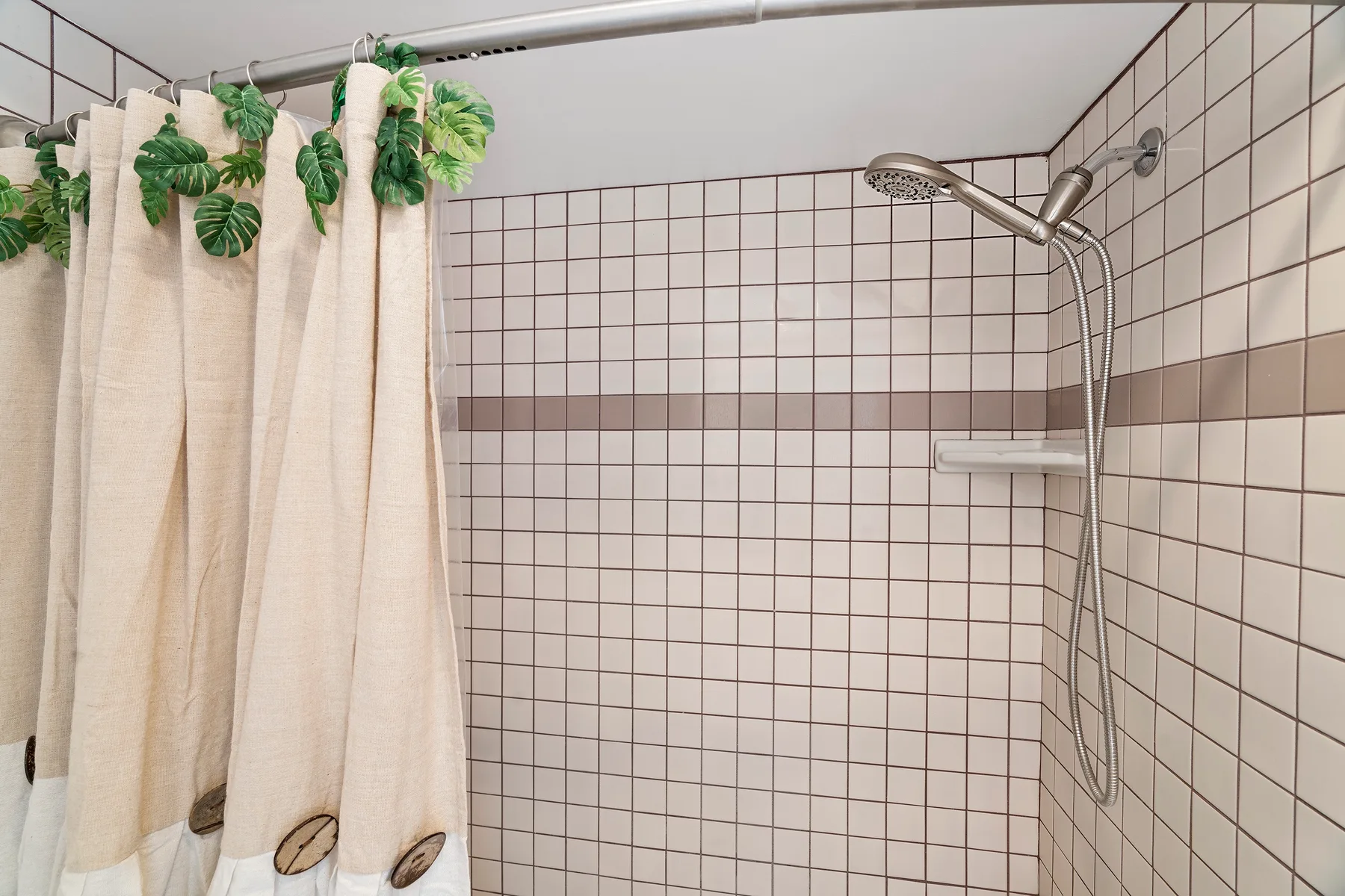 Una zona de ducha con azulejos, cortina y ducha de pared.