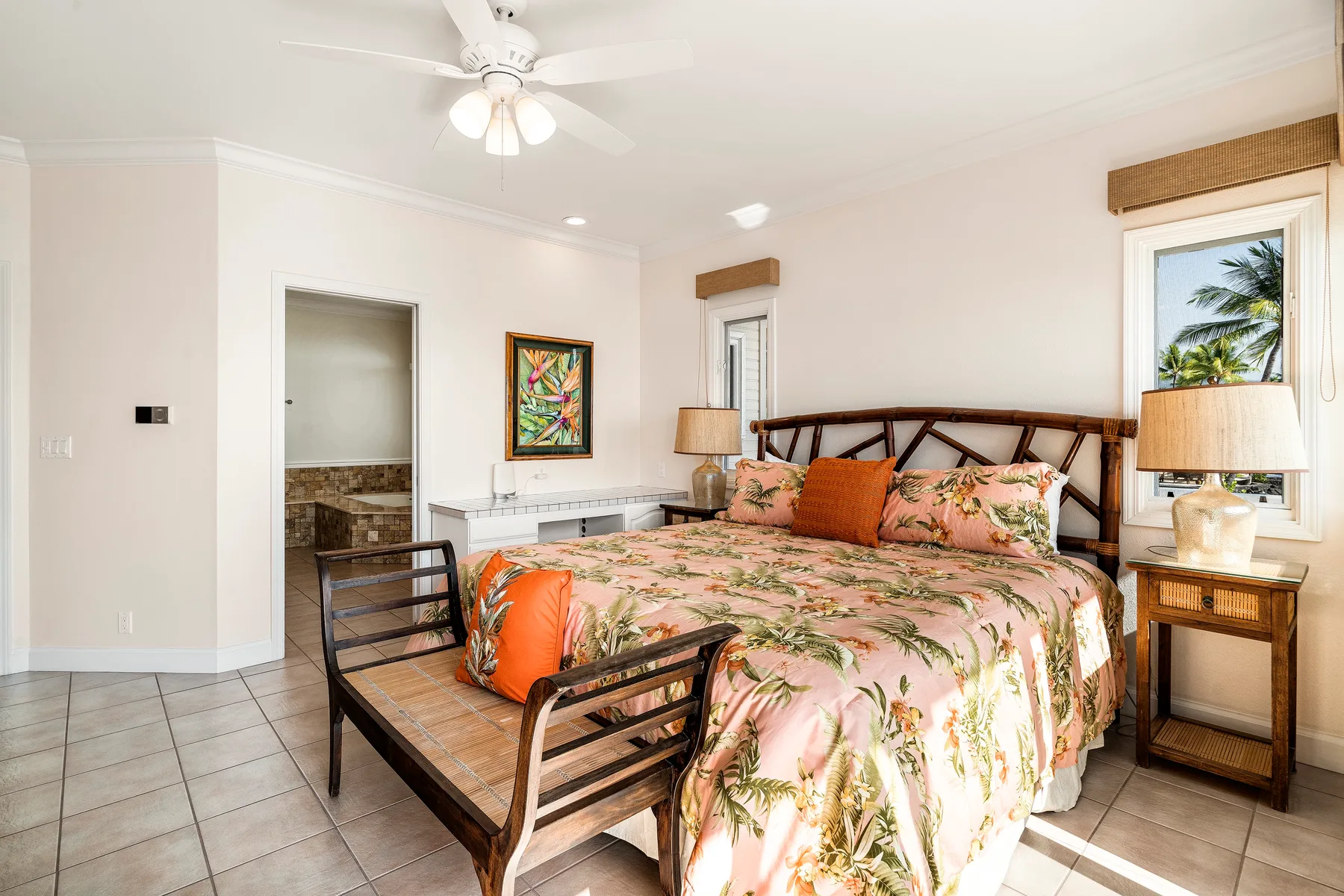 Un dormitorio luminoso con una colcha floral y un banco de madera al pie de la cama.