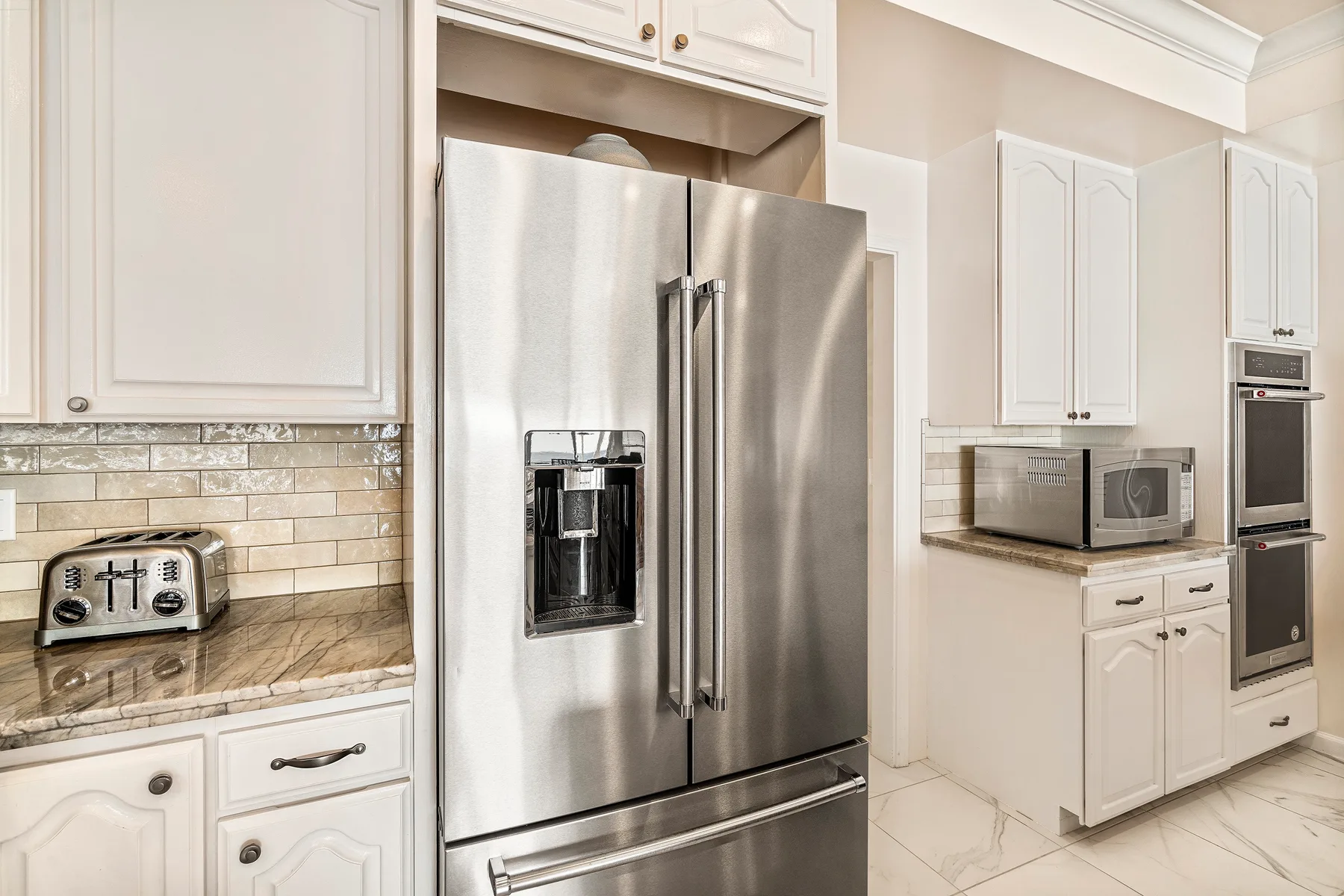 Una cocina luminosa con gabinetes blancos, un refrigerador de acero inoxidable y electrodomésticos sobre la encimera.