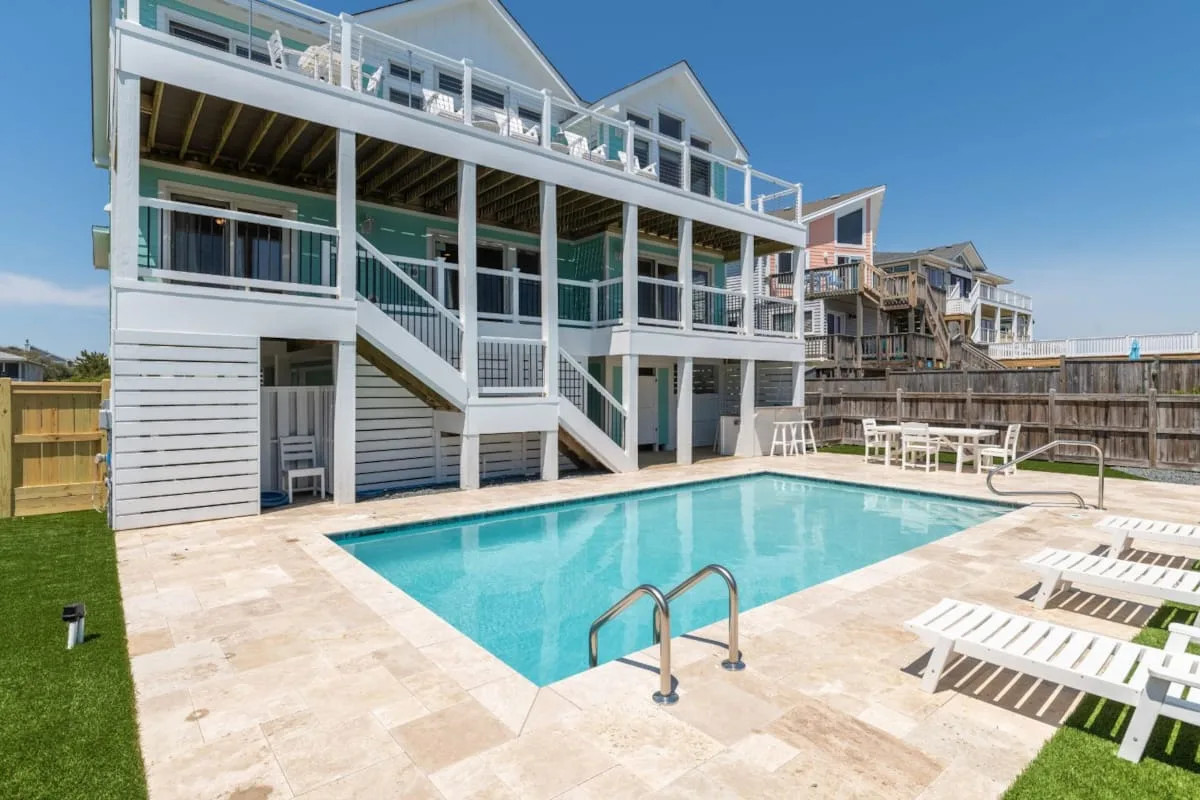 A backyard swimming pool sits beside a large white multi-level house.
