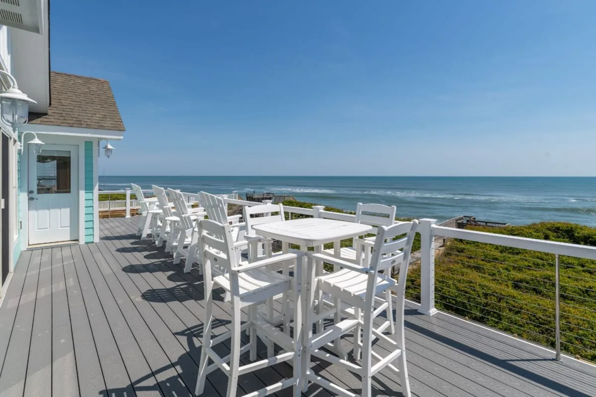 An outdoor dining deck overlooks the ocean, with white tables and seating.