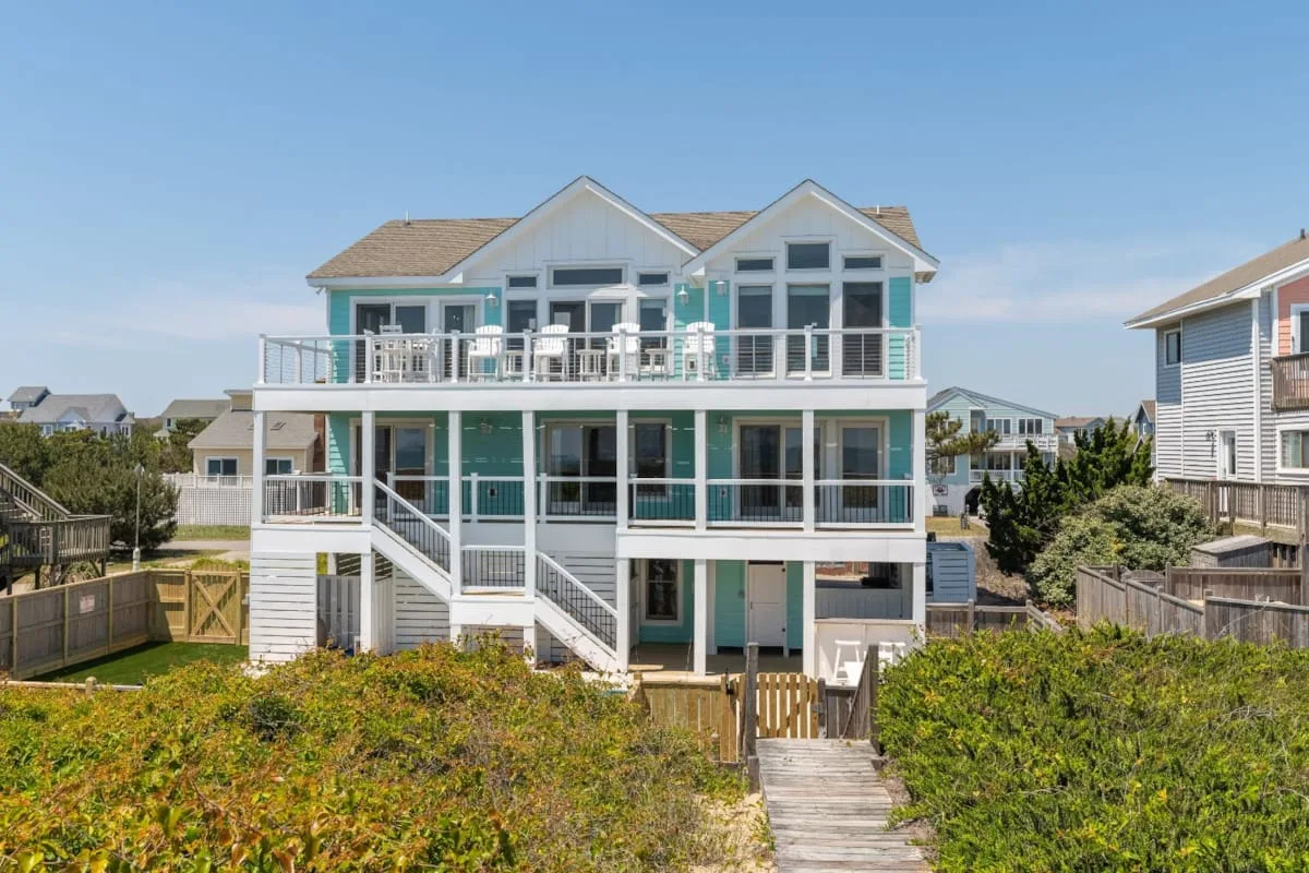 A large coastal-style house with balconies stands behind a wooden walkway.