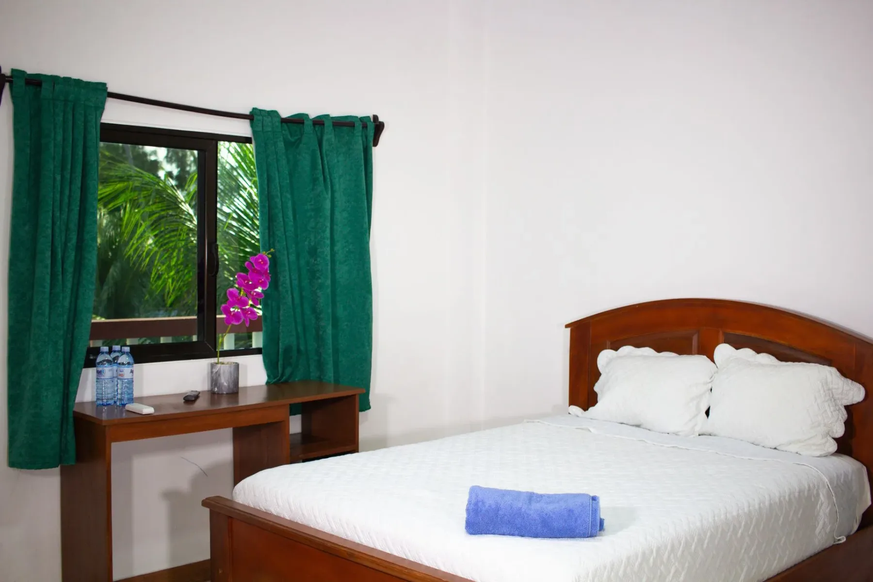 Dormitorio con cama, escritorio y ventana con cortinas verdes