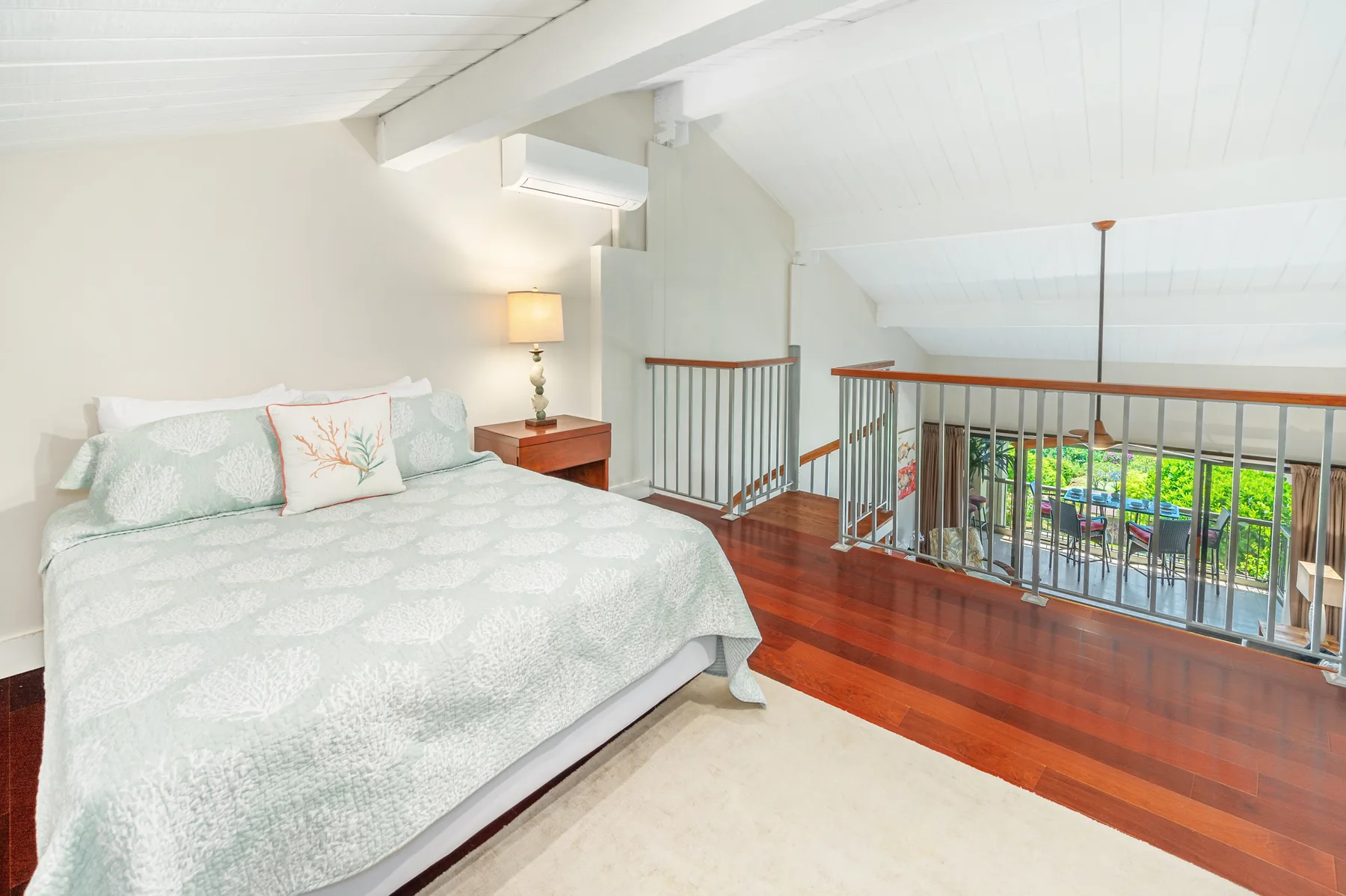 A bright bedroom with a neatly made bed beside a wooden-railed landing.