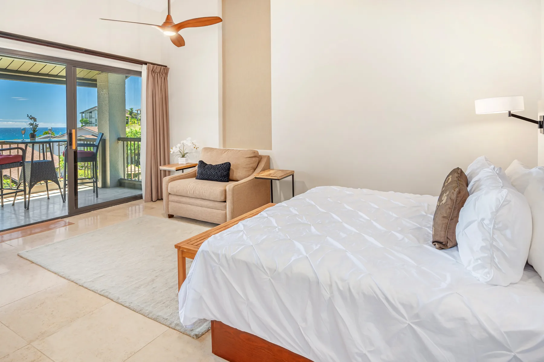 A bright bedroom with a bed, seating area, and sliding glass doors opening to a balcony.