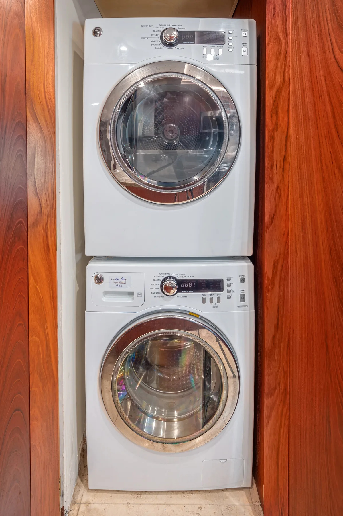 A laundry area with a stacked washer and dryer between wooden cabinets.