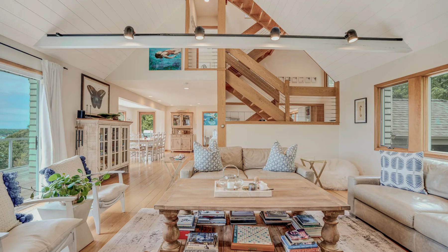 A bright living room with pale seating, a coffee table, and a wooden staircase.